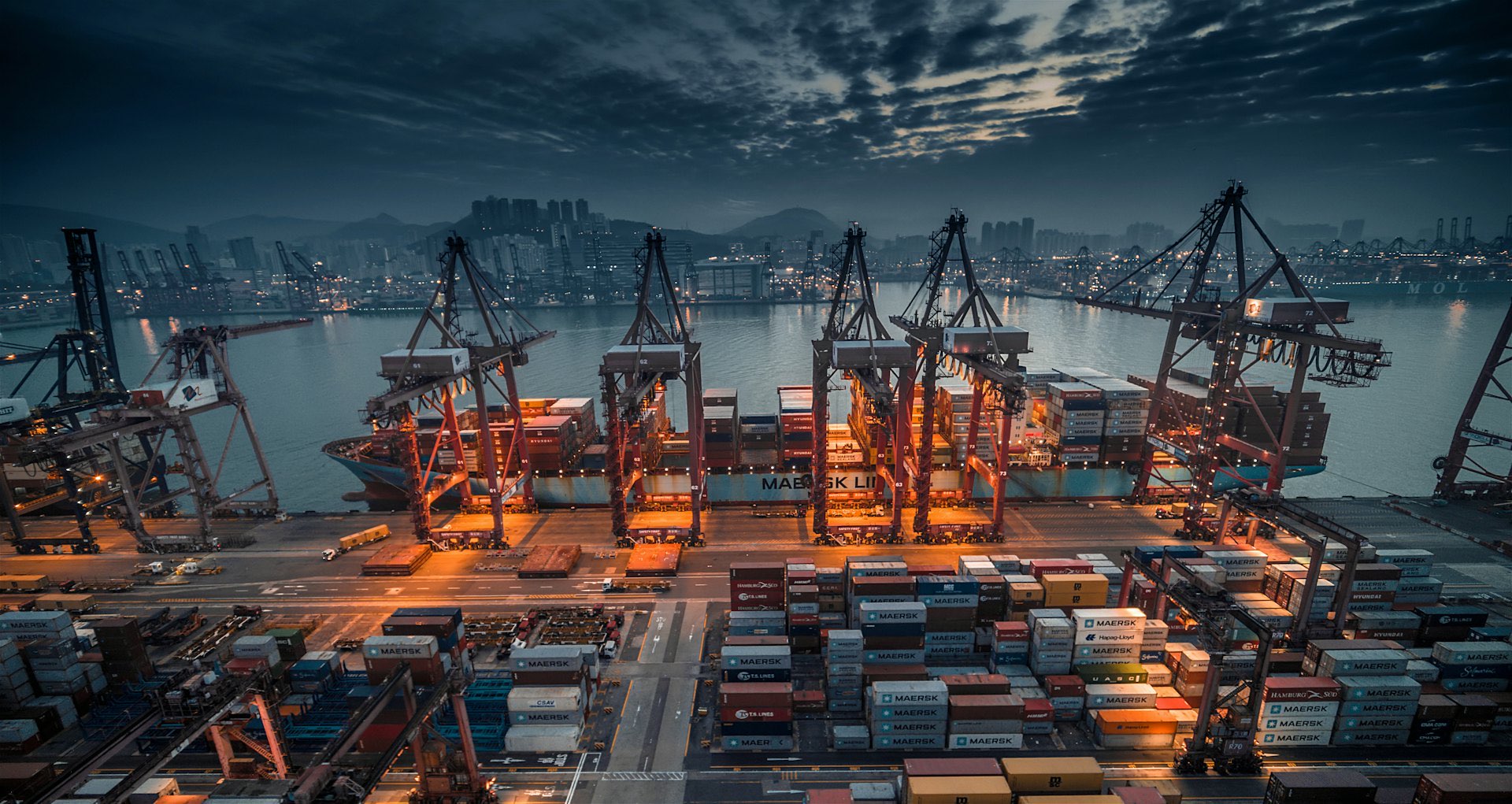 Container ship being loaded by cranes at an industrial port at dusk